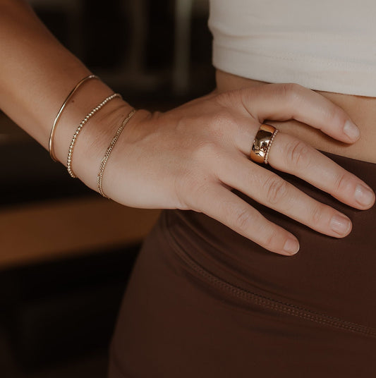 Close up of a pilates model wearing a permanent bangle, stretchy beaded bracelet, two permanent bracelets and a ring stack with a stainless steel wide band and a stretchy beaded ring