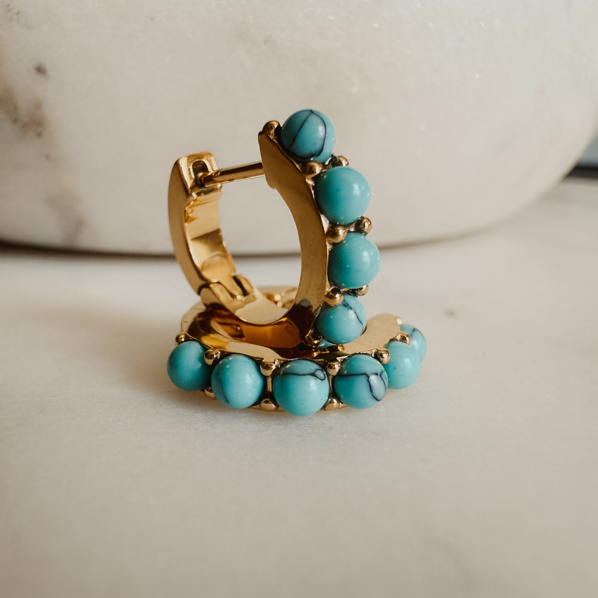 Gold hoop earring with turquoise beads on a marble surface