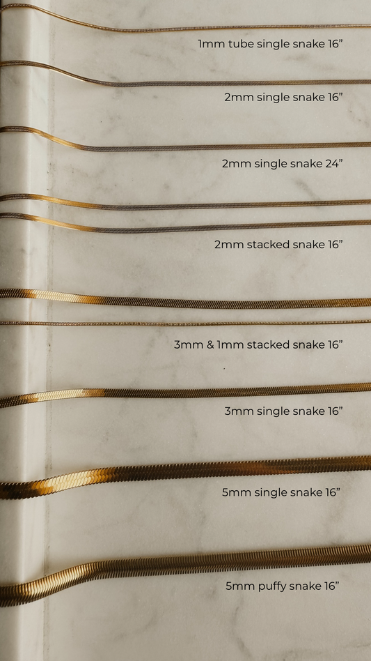 Gold snake chain shown in all different sizes and styles laid out on marble