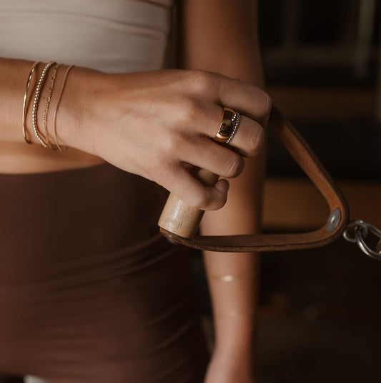 Close up of a hand holding a leather handle from a pilates reformer with gold bracelets and rings 