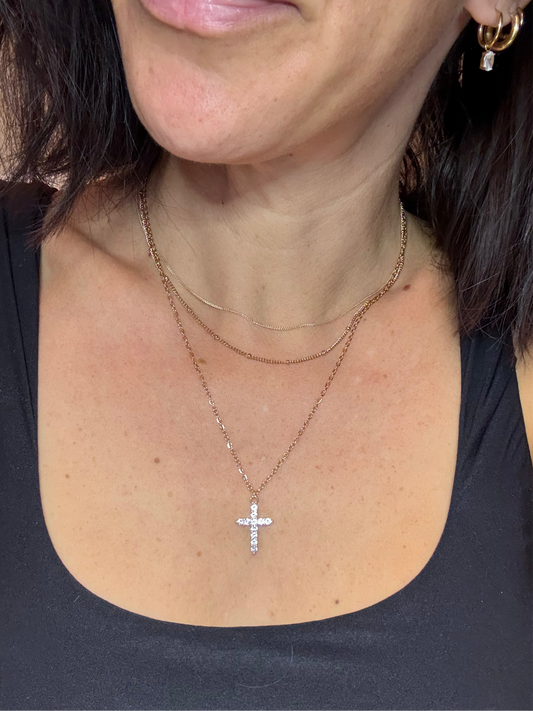 model wearing 14k solid gold necklace and a pre-stacked stainless steel cross necklace and stainless steel huggie hoop earring stack